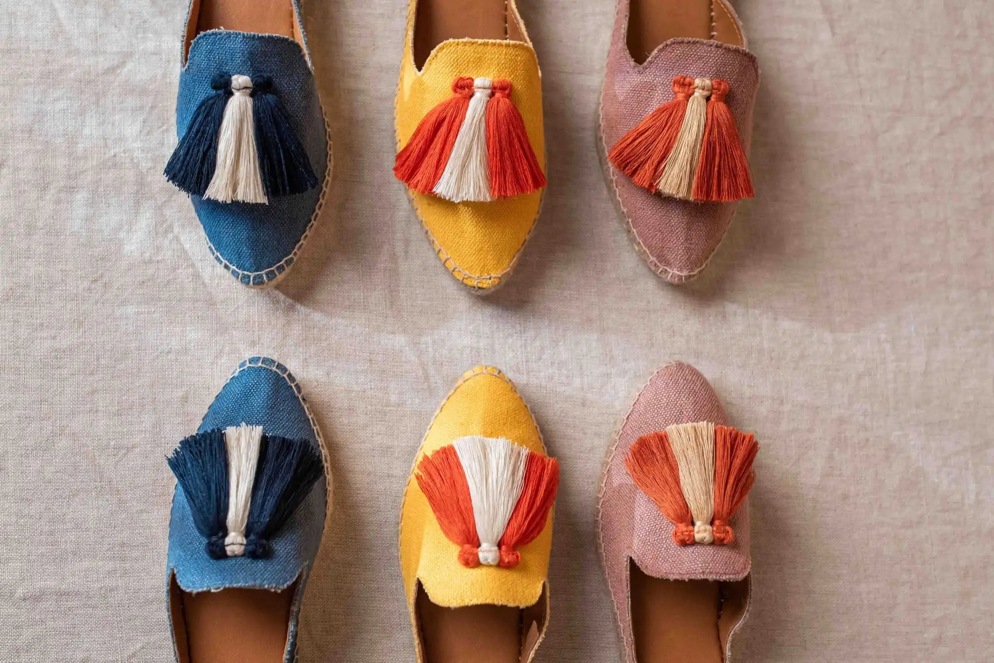 Mules de ante coloridos con borlas decorativas en azul, amarillo y rosa.